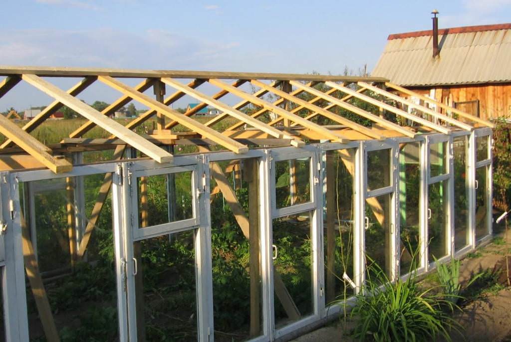 Конструкция теплицы из старых оконных рам получается достаточно тяжелой, поэтому увеличивать ее вес стеклом мы не советуем